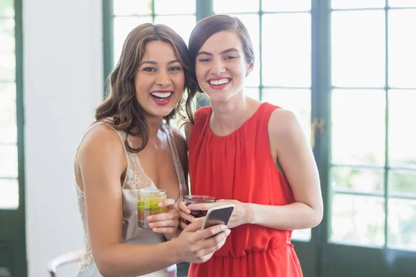 Friends with cocktail glasses laughing while using mobile phone in the restaurant — Stock Photo, Image