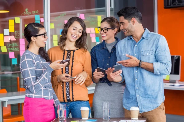 Lächelnde Führungskräfte interagieren während sie Mobiltelefone nutzen — Stockfoto