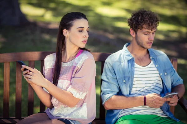 Jealous woman spying her man's mobile phone in park — Stock Photo, Image