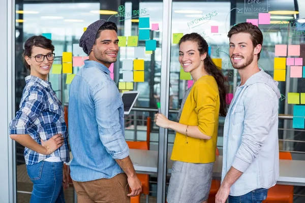 Ejecutivos sonrientes discutiendo sobre notas adhesivas en la pared de vidrio —  Fotos de Stock