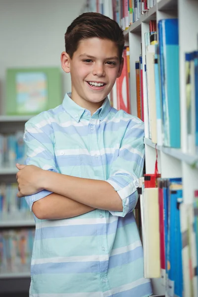 Porträtt av leende skolpojke står med armarna korsade i biblioteket — Stockfoto