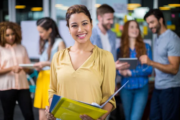 Portrait of smiling female executive holding clipboard and file — Stock Photo, Image