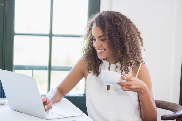 Vrouw houden koffiekopje en met behulp van de laptop in een restaurant — Stockfoto