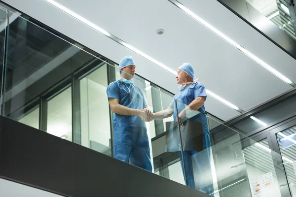 Male surgeons shaking hands in corridor — Stock Photo, Image