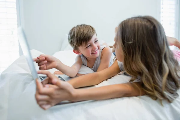 Chica y niño usando el ordenador portátil en la cama en el dormitorio —  Fotos de Stock