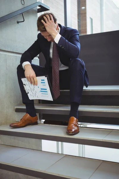 Depressed businessman with clipboard on stairs — Stock Photo, Image