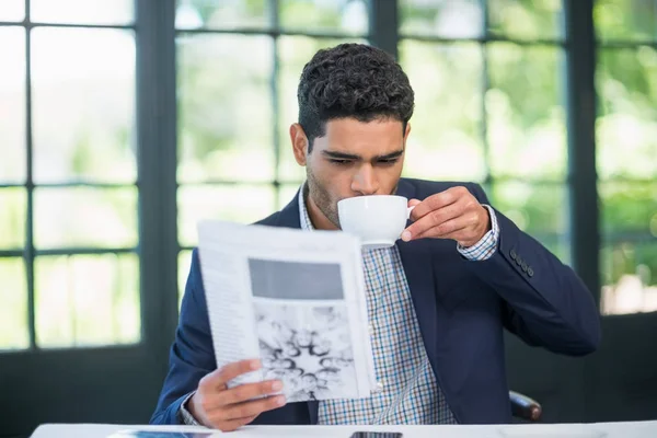 Empresario leyendo periódico mientras toma café — Foto de Stock