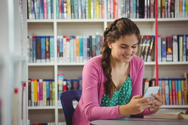 Lächelndes Schulmädchen mit Handy in Bibliothek — Stockfoto