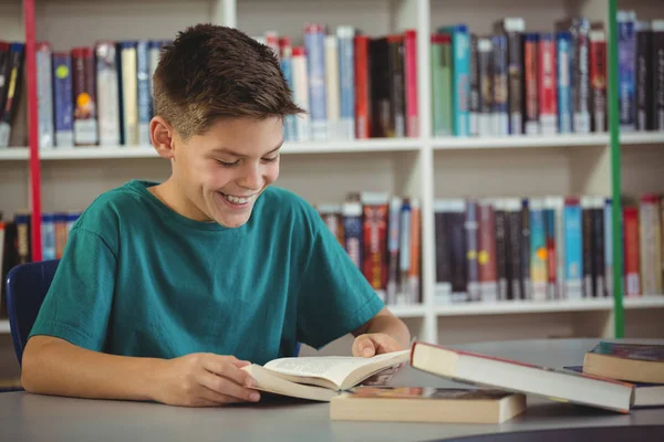 Glimlachend schooljongen leesboek in bibliotheek — Stockfoto