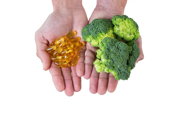 Close-up de mãos segurando brócolis e pílulas de vitaminas — Fotografia de Stock