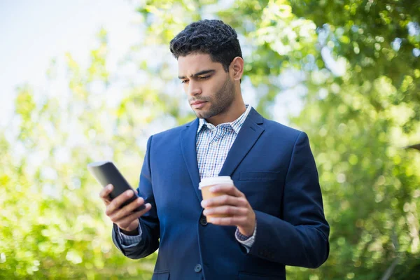 Empresario sosteniendo taza de café desechable y el uso de teléfono móvil — Foto de Stock