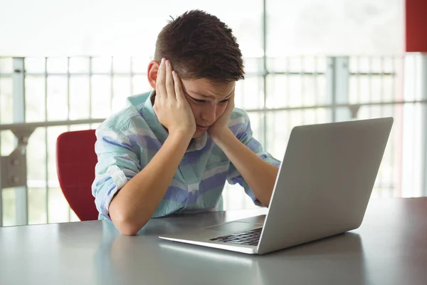 Sad schoolboy looking at laptop in library — Stock Photo, Image