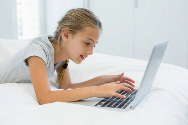 Menina deitada na cama e usando laptop no quarto — Fotografia de Stock