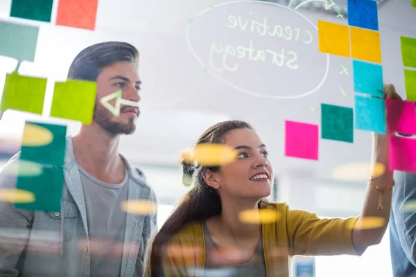 Smiling executives writing on sticky notes on glass wall — Stock Photo, Image