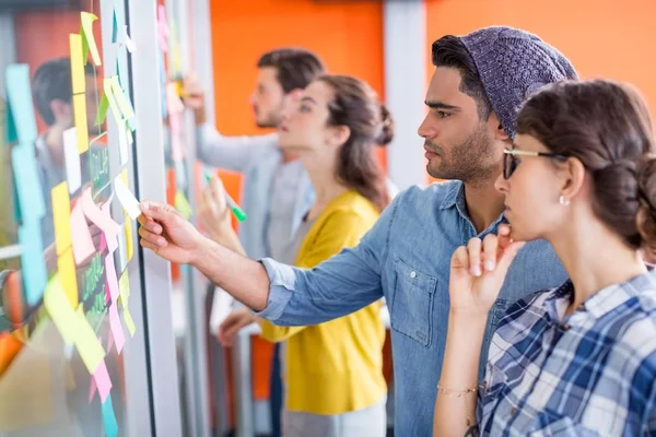 Executives reading sticky notes on glass wall — Stock Photo, Image