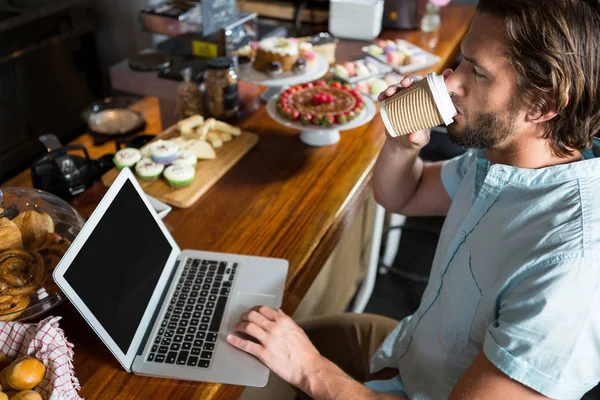 Man met koffie terwijl het gebruiken van laptop aan balie — Stockfoto