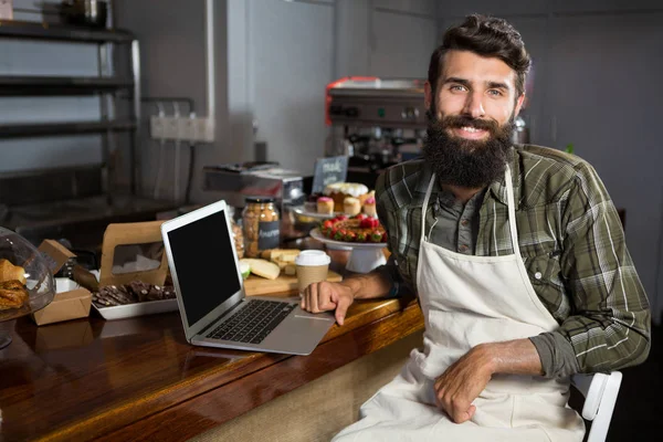 Staf pria tersenyum menggunakan laptop di counter di toko roti — Stok Foto