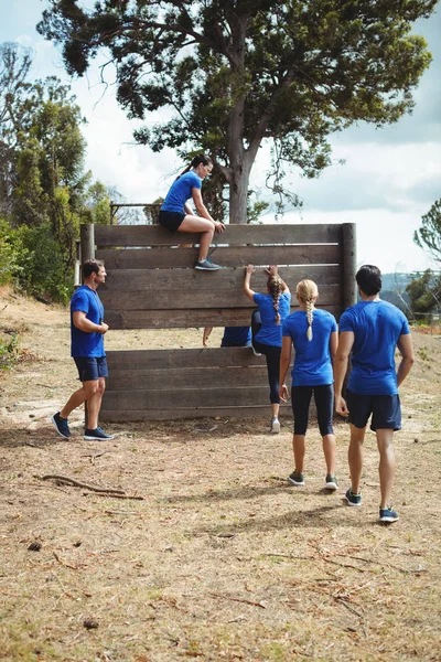 Treinador feminino ajudando a mulher em forma a subir sobre a parede de madeira durante o curso de obstáculo — Fotografia de Stock