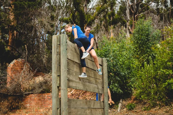 Trainerin hilft Frau beim Klettern einer Holzwand — Stockfoto