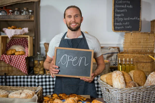 Portrait of smiling staff holding chalkboard with open sign at counter — Stock Photo, Image