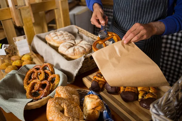 Mid section of staff packing croissant in paper bag at counter — Stock Photo, Image