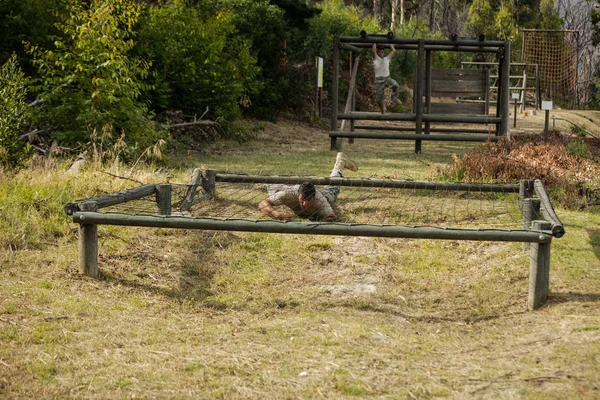 Soldado rastejando sob a rede durante o curso de obstáculo — Fotografia de Stock