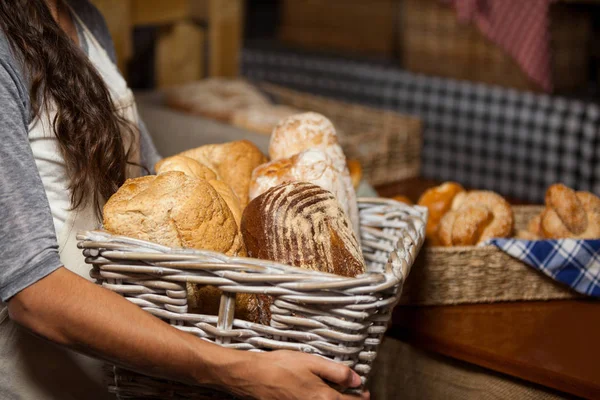 パン屋さんのカウンターでいろいろなパンの枝編み細工品バスケットを保持している女性スタッフ — ストック写真