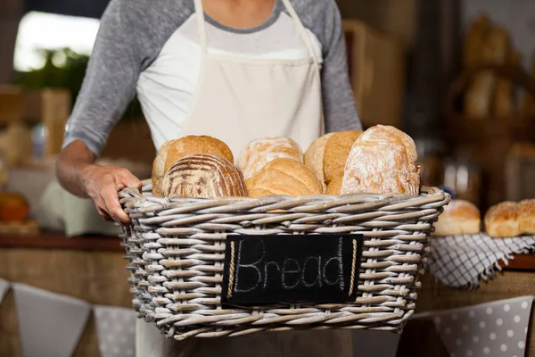 Vrouwelijk personeel houden rieten mand van verschillende broden op de teller in bakkerij winkel — Stockfoto