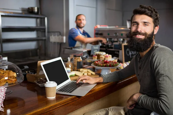Cliente masculino usando laptop enquanto toma café no balcão no café — Fotografia de Stock