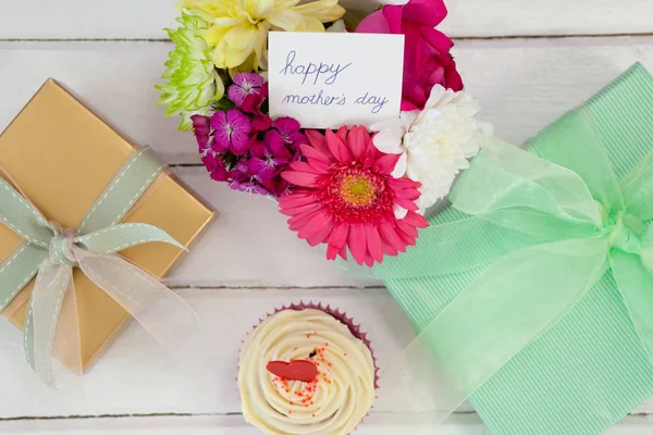 Cup cake, doos van de gift en verse bloemen op houten oppervlak — Stockfoto