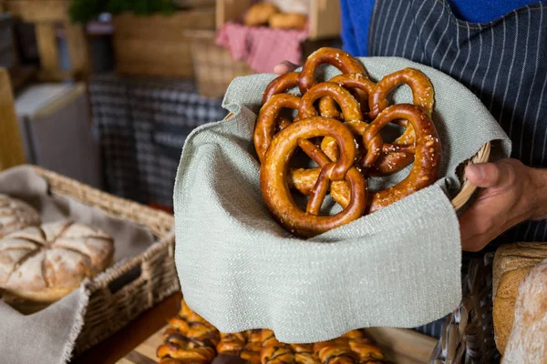 Mid section of staff holding wicker basket of pretzel breads at counter — Stock Photo, Image