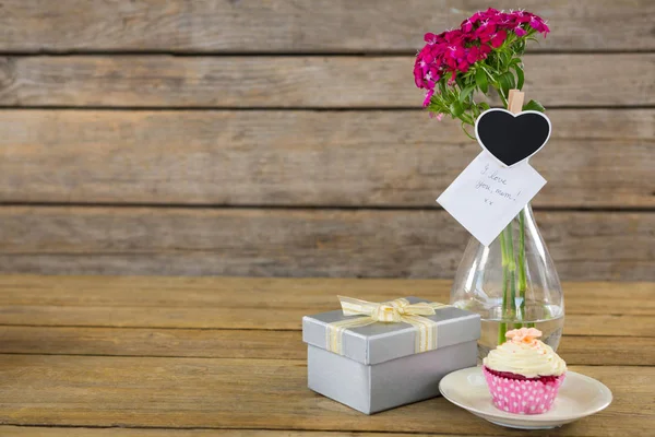 Geschenkkarton und Blumenvase mit Cupcake im Teller auf Holzplanke — Stockfoto