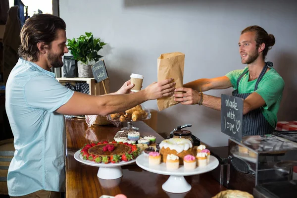 Cliente sonriente recibiendo un paquete del personal en el mostrador — Foto de Stock