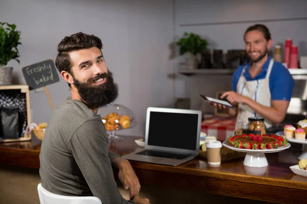 Mužských zákazníků pomocí přenosného počítače zároveň s kávou u přepážky v kavárně — Stock fotografie