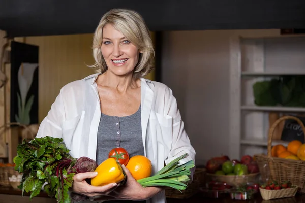 Portrait femme costumière tenant légumes et fruits frais en section bio — Photo