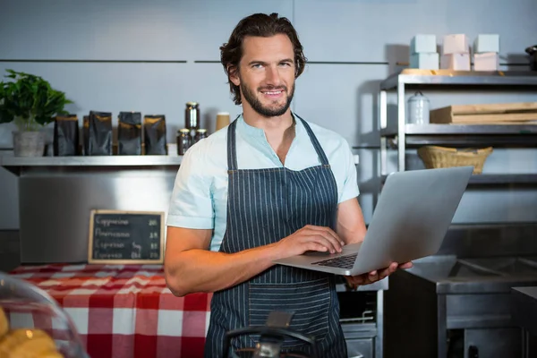 Sorridente personale maschile utilizzando il computer portatile al bancone — Foto Stock