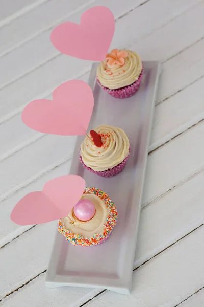 Primer plano de tres deliciosos cupcakes con tarjetas en forma de corazón en bandeja — Foto de Stock