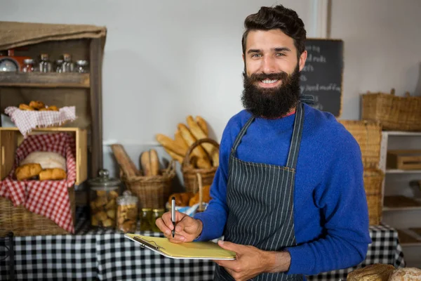 Glimlachende man personeel schrijven op Klembord aan balie in bakkerij winkel — Stockfoto