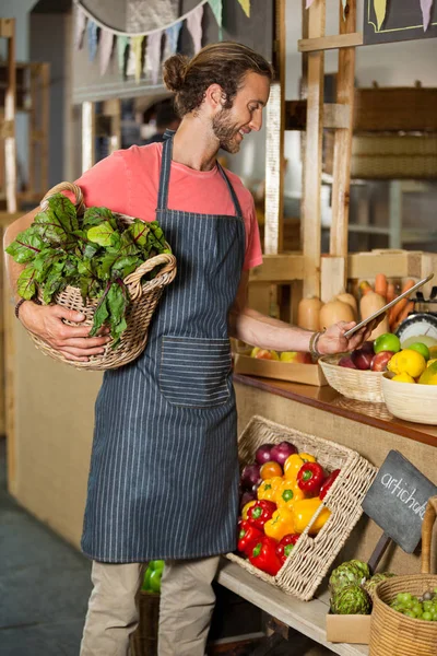 Personnel masculin tenant des légumes feuillus et utilisant une tablette numérique dans la section biologique — Photo