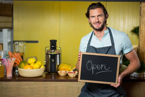 Smiling shop assistant holding a board with open sign — Stock Photo, Image