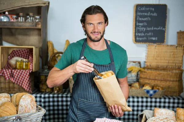 Portrait of male staff packing bread in paper bag — Stock Photo, Image