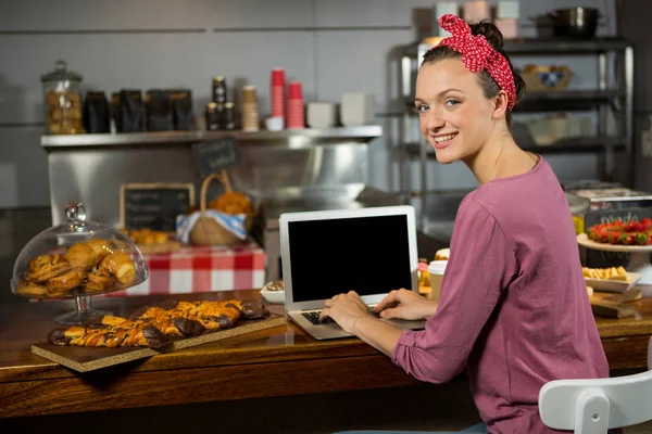 Mulher usando laptop no balcão de padaria no mercado — Fotografia de Stock