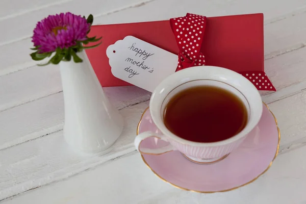 Svart te, blomvas och glad mödrar dag kort på träytan — Stockfoto