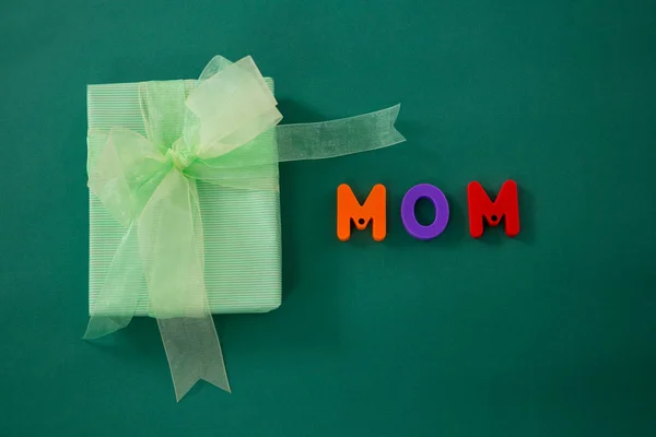 Gift box with alphabets displaying mom against green background — Stock Photo, Image