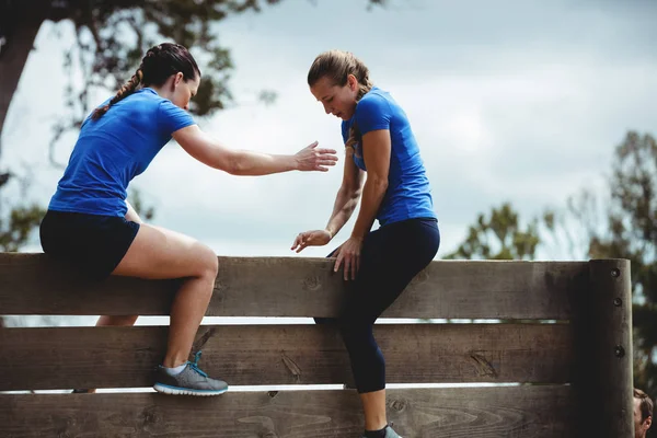 Entraîneur féminin aidant la femme à escalader un mur en bois — Photo