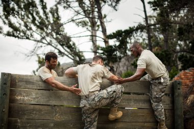 Soldiers helping man to climb wooden wall clipart