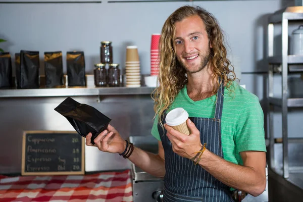 Potret staf laki-laki memegang cangkir kopi dan tas paket di counter — Stok Foto