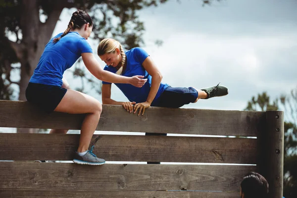 Trainerin hilft Frau beim Klettern einer Holzwand — Stockfoto