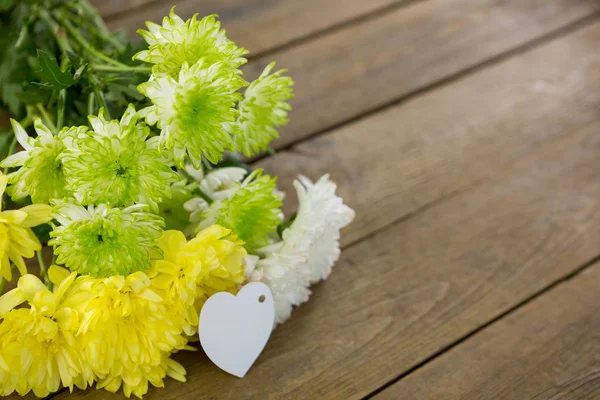 Bunch of yellow flowers with heart shape tag on wooden plank — Stock Photo, Image