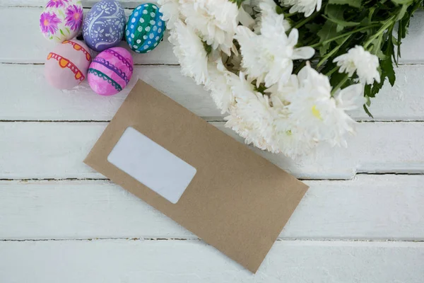 Ovos de Páscoa multicoloridos, cacho de flores e envelope — Fotografia de Stock
